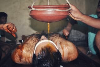 Warm herbal oil flowing during a Shirodhara treatment